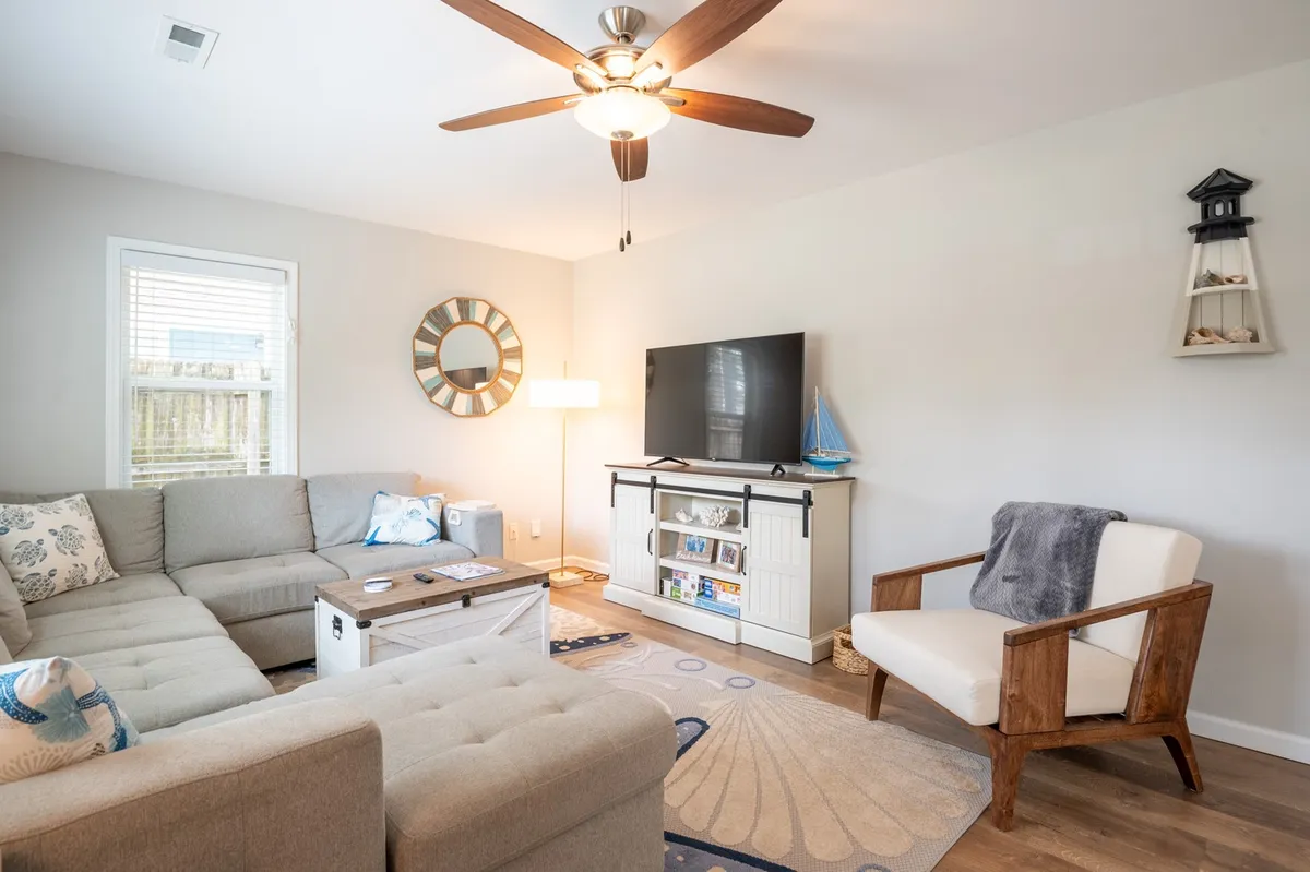 A cozy living room centered around a plush sectional sofa, a coffee table, a wall-mounted TV, and a wooden chair. The space is decorated with a modern mirror and bright touches, creating an inviting environment for relaxation and socializing.