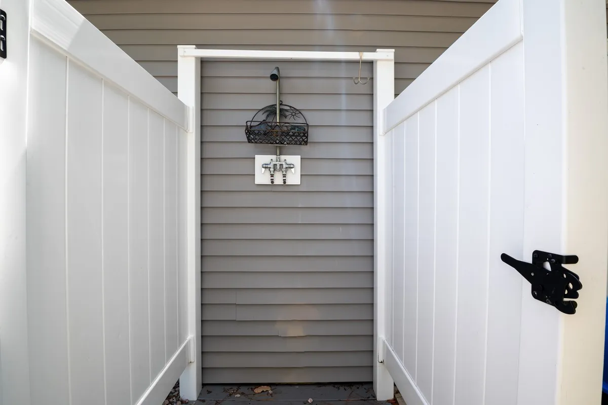 This image focuses on the outdoor shower area, featuring a stylish wooden enclosure and a decorative basket. The fence provides privacy, and greenery peeks over the top, enhancing the refreshing outdoor feel.