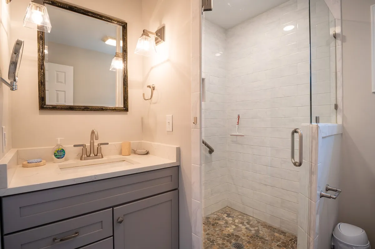 A well-lit bathroom featuring a modern vanity sink, a framed mirror, a shower area, and stone flooring. The ambiance is serene and inviting, ideal for freshening up before heading out or relaxing after returning from adventures.