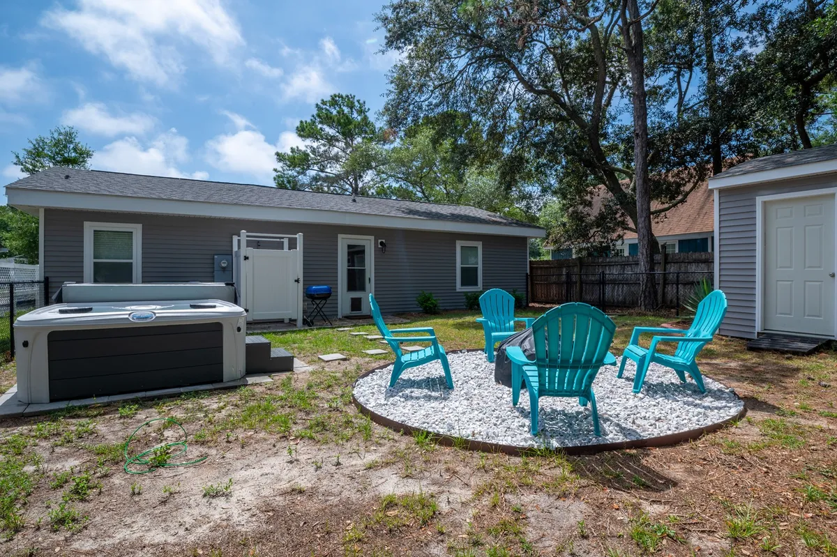 This image displays a well-designed backyard featuring a spacious hot tub, a fire pit area surrounded by Adirondack chairs, and lush greenery. The setup emphasizes areas for relaxation, socializing, and enjoying the outdoors with friends or family. The fire pit and hot tub are prominent, and the yard feels inviting and private.