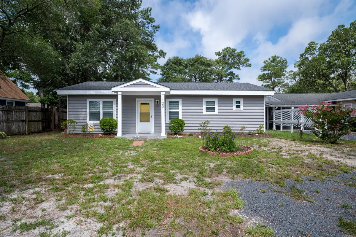 The image shows the welcoming exterior of Beach Break Bungalow, featuring a charming front door framed by lush landscaping and big windows. The inviting porch hints at space for morning coffee or evening relaxation, with a fenced yard ideal for pets and family gatherings. Soft lighting and well-kept surroundings create an atmosphere that feels both cozy and vibrant—perfect for a beach getaway.